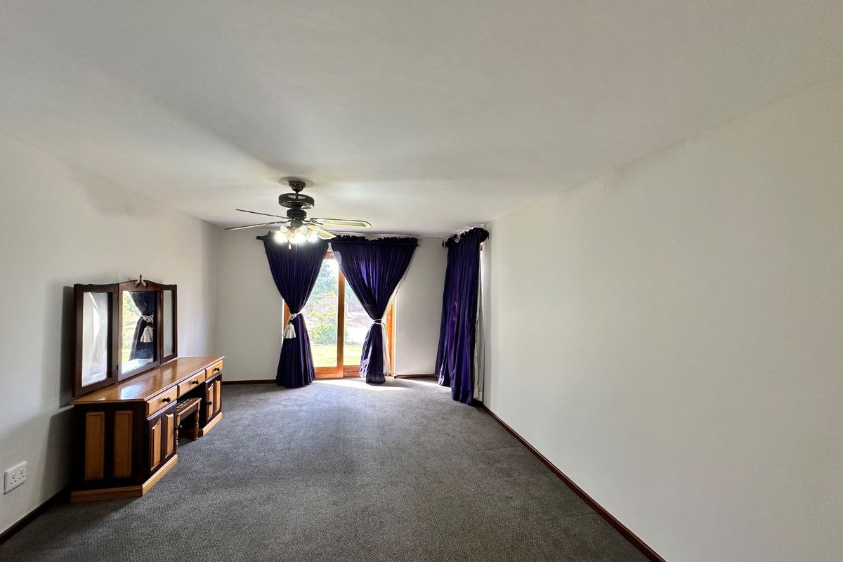 A spacious bedroom featuring neutral walls, carpeted flooring, a ceiling fan, and a sliding glass door providing access to the exterior.