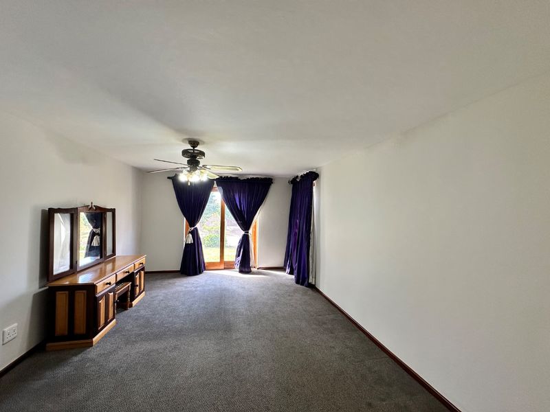 A spacious bedroom featuring neutral walls, carpeted flooring, a ceiling fan, and a sliding glass door providing access to the exterior.