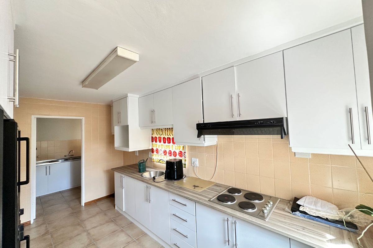 A functional kitchen featuring white cabinetry, laminate countertops, an electric hob with extractor fan, and tiled backsplash, with an adjacent scullery area visible.