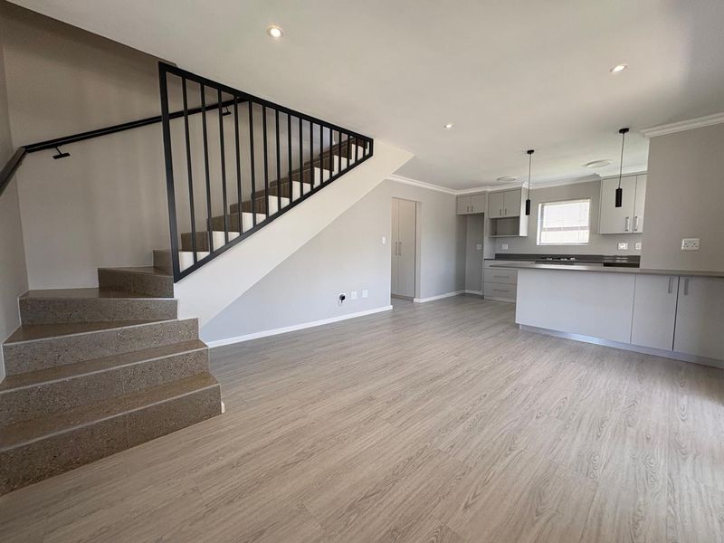 Modern open-plan living area featuring laminate flooring, a sleek staircase with metal balustrade, and a contemporary kitchen with built-in cabinetry and island.