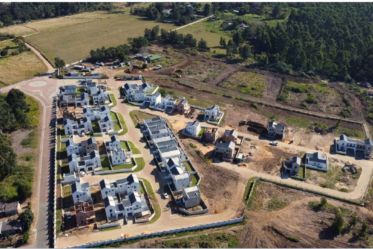 Aerial view of a residential housing development estate showing multiple completed and under-construction units with paved access roads and perimeter fencing.