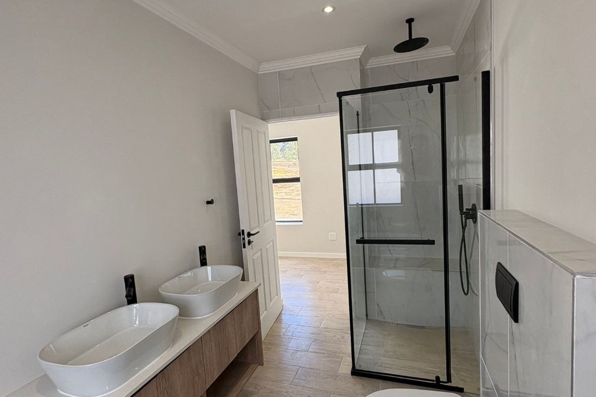Modern bathroom featuring a double vanity with vessel sinks, a walk-in shower with black fixtures, and a wall-hung toilet with marble-look tiling.