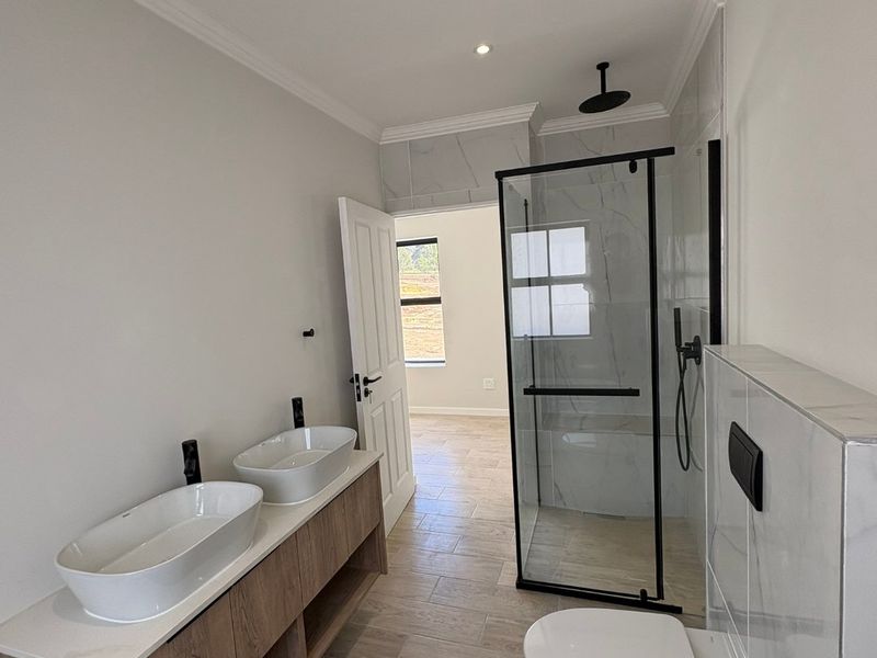 Modern bathroom featuring a double vanity with vessel sinks, a walk-in shower with black fixtures, and a wall-hung toilet with marble-look tiling.