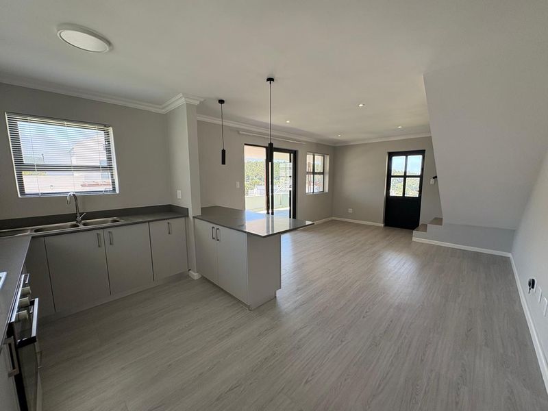 Spacious open-plan living area featuring a modern kitchen with built-in cabinetry, an island, and seamless flow to the outdoor patio through sliding glass doors.