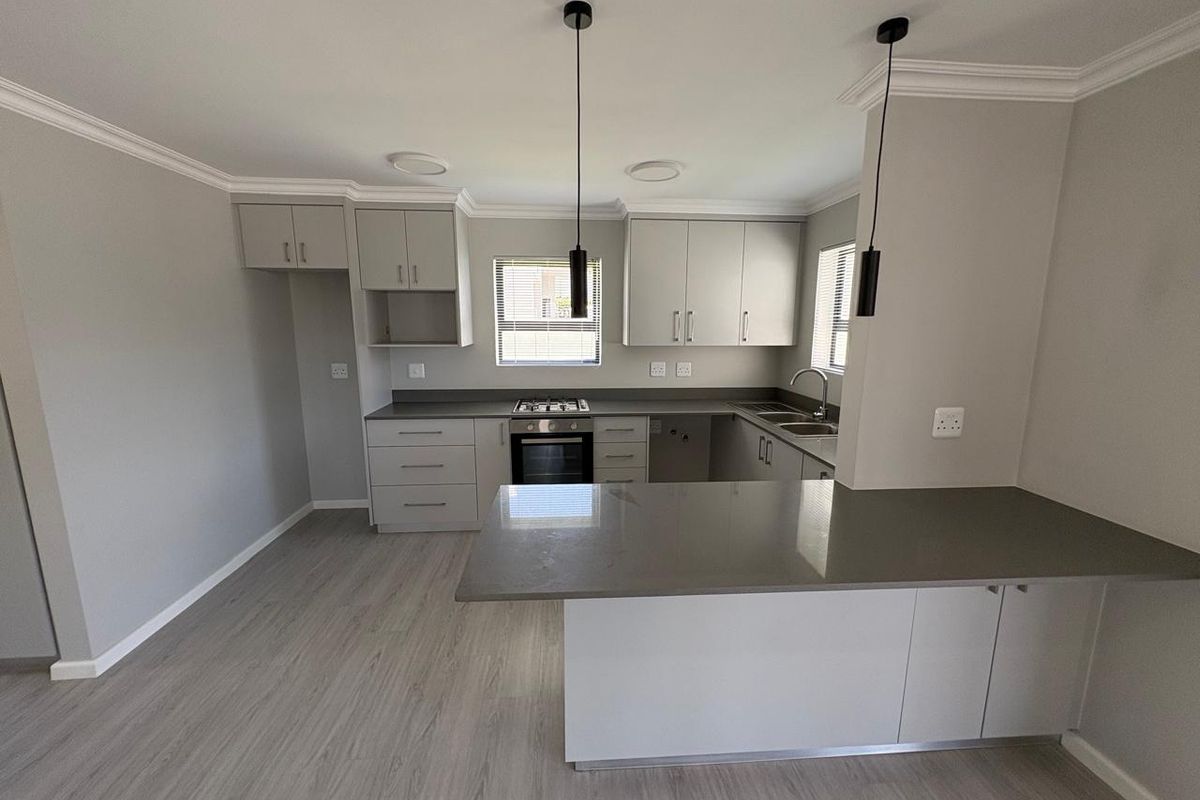Modern, clean-lined kitchen featuring neutral cabinetry, stone countertops, integrated gas hob and oven, and a functional breakfast bar island.