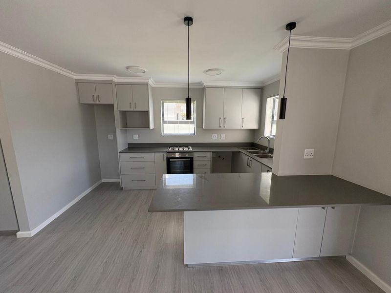 Modern, clean-lined kitchen featuring neutral cabinetry, stone countertops, integrated gas hob and oven, and a functional breakfast bar island.