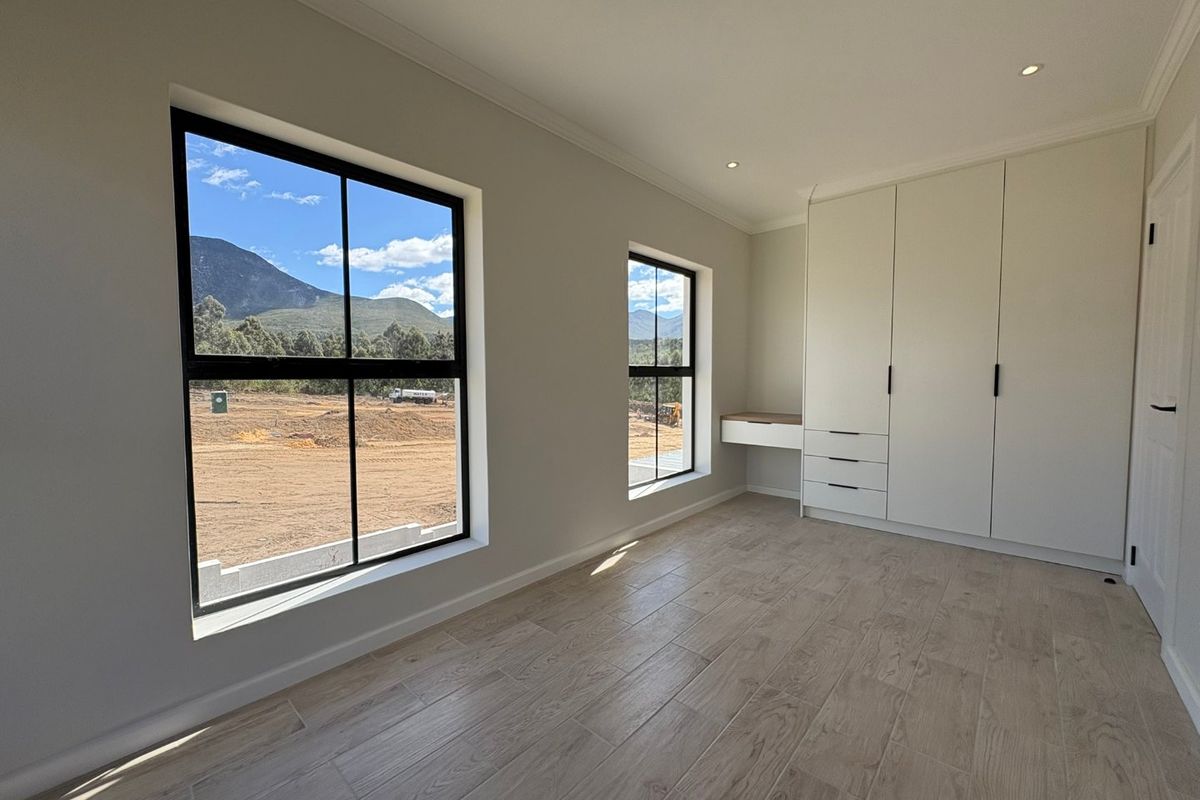 A bright, modern bedroom featuring built-in cupboards, an integrated desk, tiled flooring, and large windows with scenic mountain views.