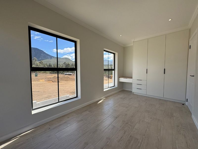 A bright, modern bedroom featuring built-in cupboards, an integrated desk, tiled flooring, and large windows with scenic mountain views.