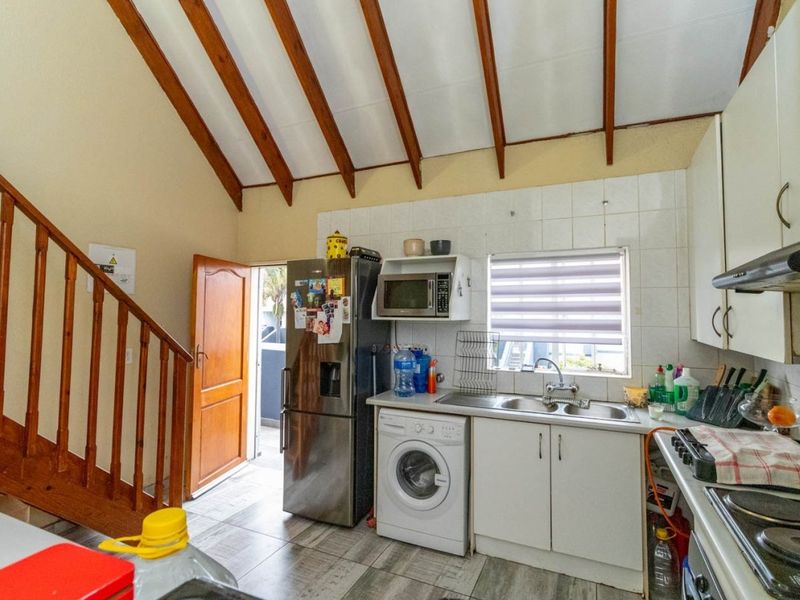 Compact kitchen featuring exposed timber ceiling beams, tiled splashback, stainless steel sink, and integrated cabinetry, with an adjacent staircase leading to the upper level.