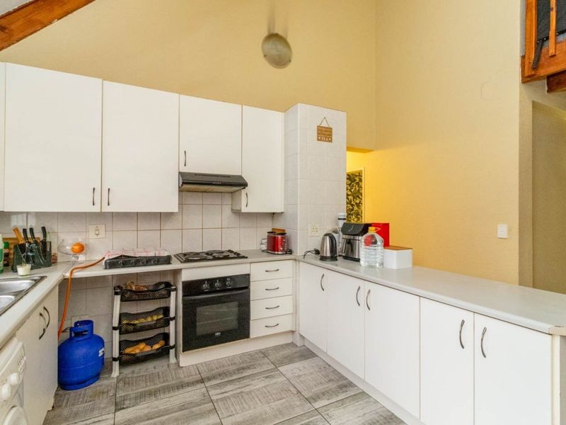 Functional kitchen featuring white cabinetry, built-in oven, gas hob, extractor fan, and tiled flooring, set under a high vaulted ceiling.