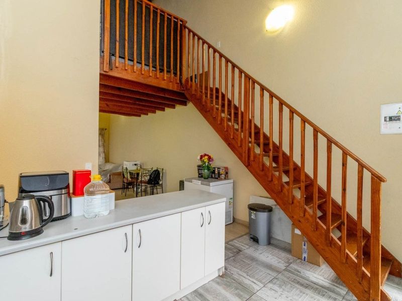 Open plan living area featuring a wooden staircase with balustrade, kitchen cabinetry, and tiled flooring, providing a functional layout for the townhouse.