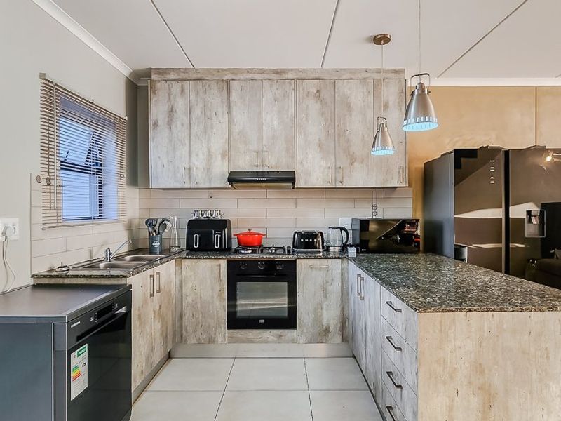 Modern open-plan kitchen featuring wood-look cabinetry, granite countertops, built-in oven, gas hob, and tiled flooring, seamlessly integrated with the living area.