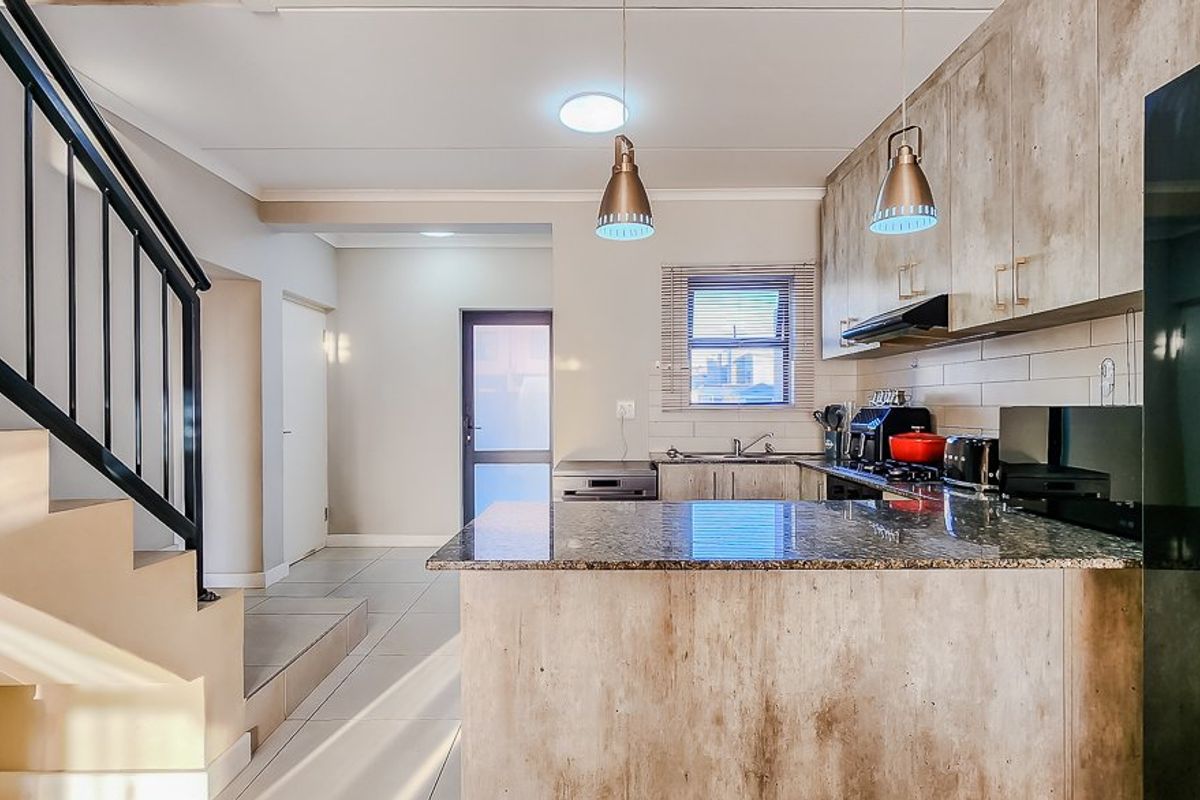 Modern kitchen featuring granite countertops, ample built-in cabinetry, and an integrated extractor fan, seamlessly connected to the staircase area with tiled flooring throughout.