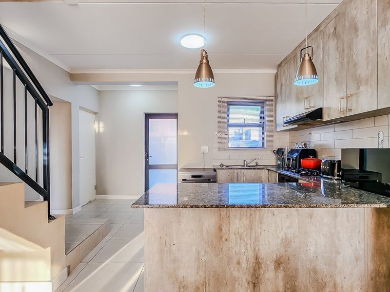 Modern kitchen featuring granite countertops, ample built-in cabinetry, and an integrated extractor fan, seamlessly connected to the staircase area with tiled flooring throughout.