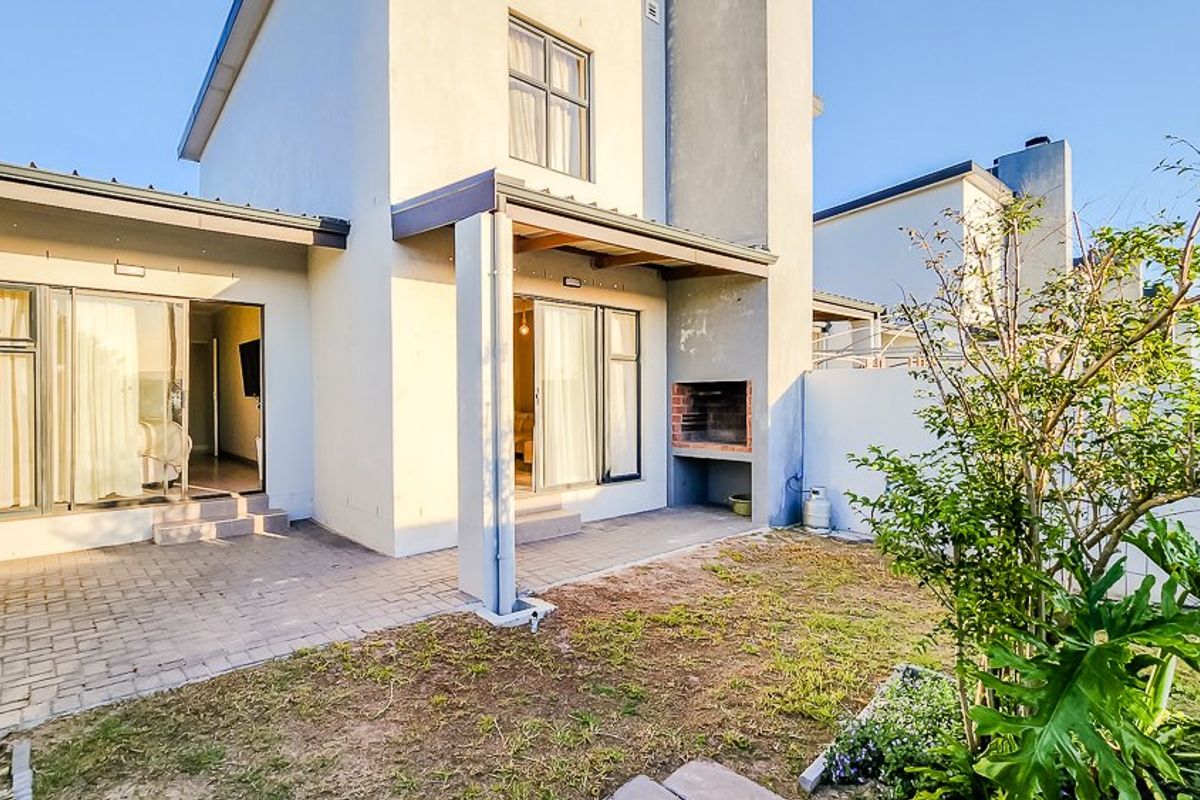 Rear exterior view of the townhouse featuring a paved patio area with a built-in braai and direct access to the interior via sliding doors.
