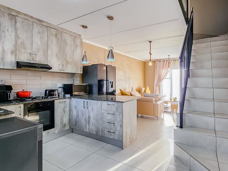 Modern open-plan kitchen and living area featuring contemporary cabinetry, tiled flooring, and an integrated staircase leading to the upper level.