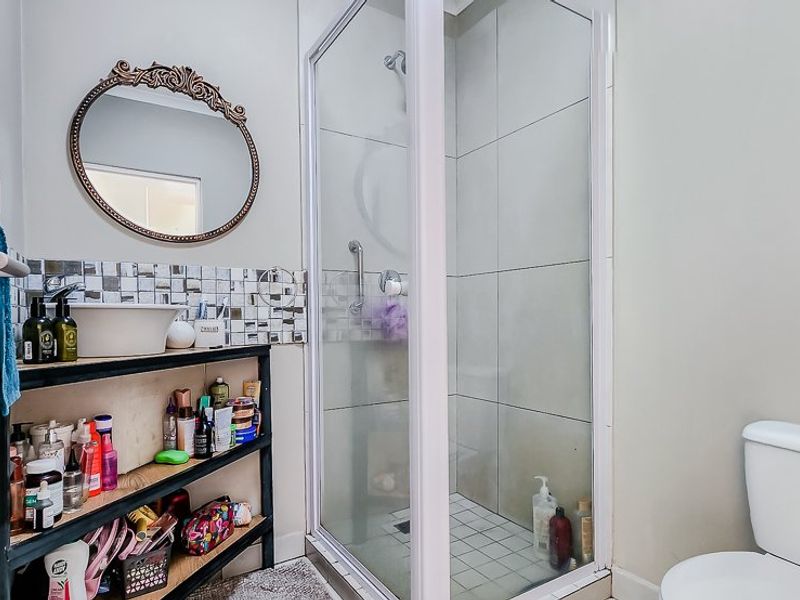A functional bathroom featuring a glass-enclosed shower, a modern vessel sink with mosaic tile backsplash, and a standard toilet.