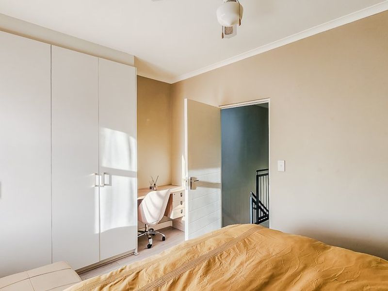 A well-lit bedroom featuring neutral walls, a built-in wardrobe, and a convenient integrated desk area.