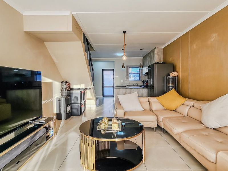 Open-plan living area featuring tiled flooring, a staircase, and an integrated kitchen space with cabinetry and sink, offering a functional layout.