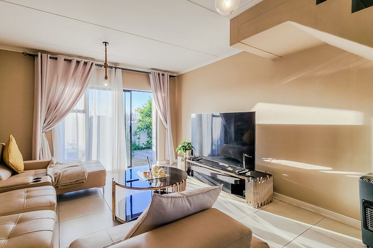 A bright and modern living room featuring tiled flooring, a staircase, and a large sliding glass door providing access to the outdoor area.
