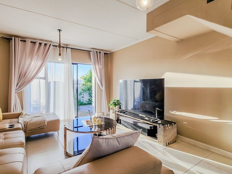 A bright and modern living room featuring tiled flooring, a staircase, and a large sliding glass door providing access to the outdoor area.