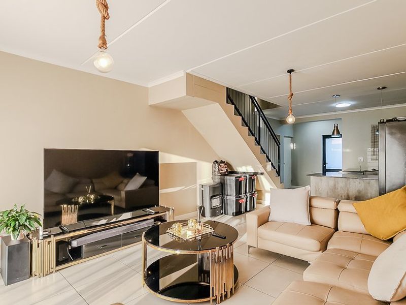 Open-plan living area featuring tiled flooring, a staircase, and integrated kitchen space, offering a functional and connected layout.