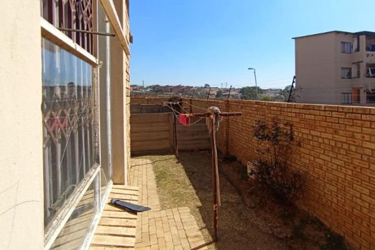 A private rear courtyard featuring a paved walkway, brick boundary walls with electric fencing, and security bars on the window.