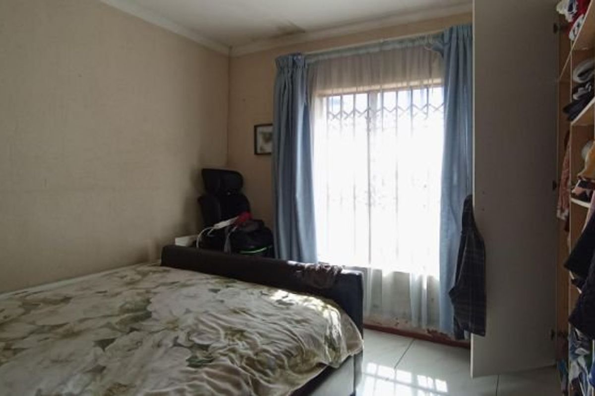 A bedroom featuring tiled flooring, a built-in wardrobe, and a window fitted with a security gate.