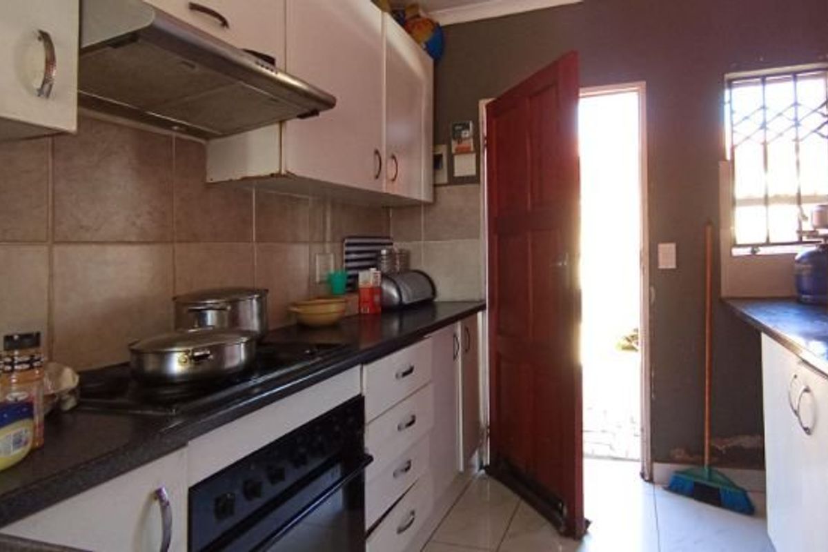Compact kitchen featuring built-in cabinetry, a hob, oven, and extractor fan, with direct access to an exterior area through a security door.