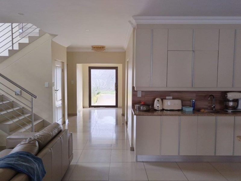 Open plan living area featuring a modern kitchen with granite countertops, tiled flooring, and a staircase with a contemporary metal balustrade.