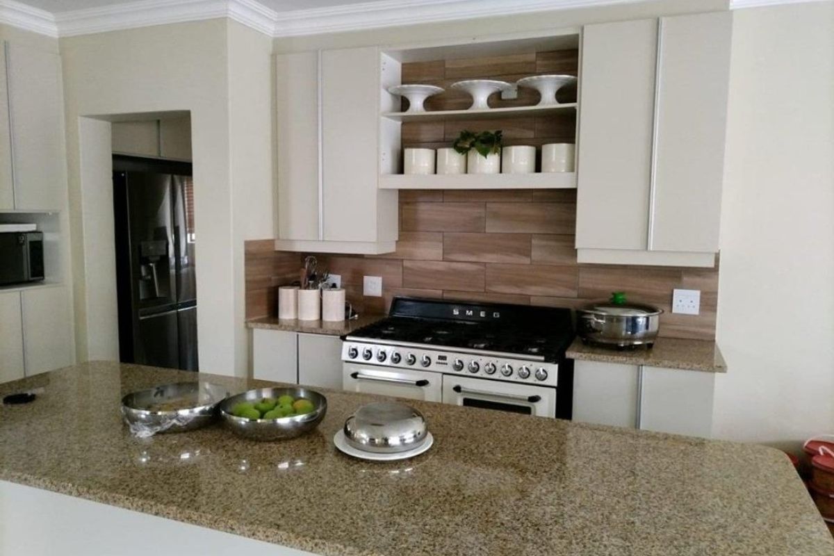 Modern kitchen featuring granite countertops, a Smeg gas stove, tiled backsplash, and ample built-in cabinetry with integrated shelving.