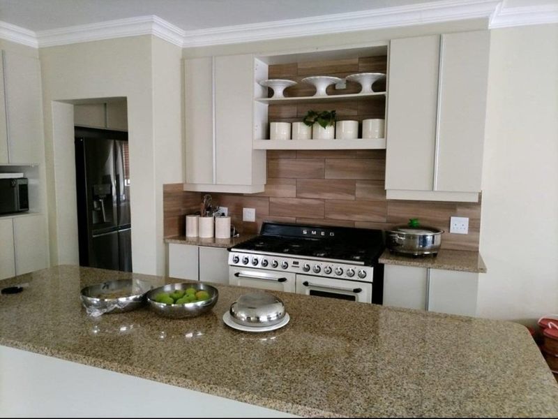 Modern kitchen featuring granite countertops, a Smeg gas stove, tiled backsplash, and ample built-in cabinetry with integrated shelving.