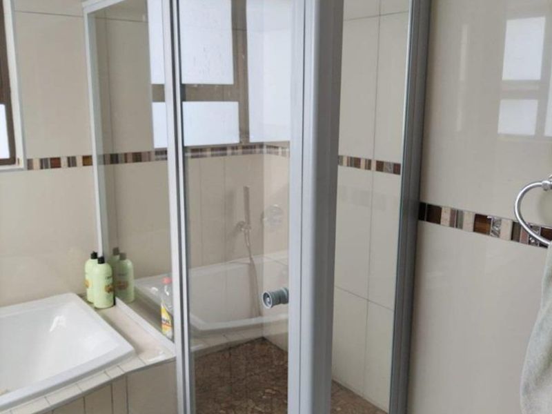 A functional bathroom featuring a glass shower enclosure, a built-in bathtub, and neutral ceramic wall tiles with a decorative mosaic border.