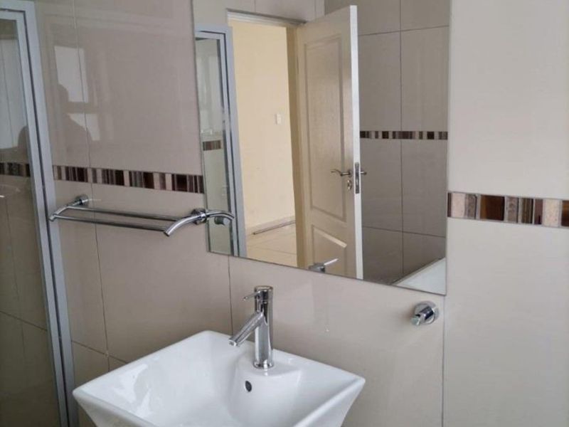 A clean, modern bathroom featuring a vessel sink on a granite vanity top, chrome fixtures, and neutral wall tiling with a decorative accent border.