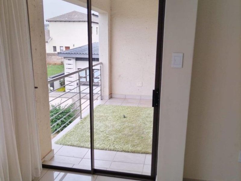 A covered balcony featuring tiled flooring and a metal balustrade, accessible through a sliding glass door from the interior living space.