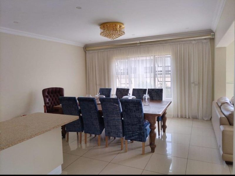 Spacious dining area featuring polished porcelain floor tiles, a central crystal chandelier, and a granite-topped breakfast bar, creating a bright and elegant atmosphere.