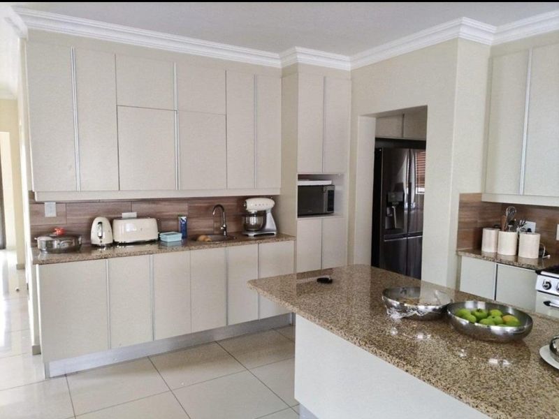 Modern kitchen featuring granite countertops, ample built-in cabinetry, tiled splashbacks, and a functional island layout with integrated appliances.