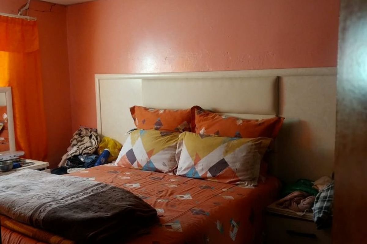 A bedroom featuring a built-in headboard and drop ceiling, showing signs of wear including wall cracking and ceiling panel irregularities.