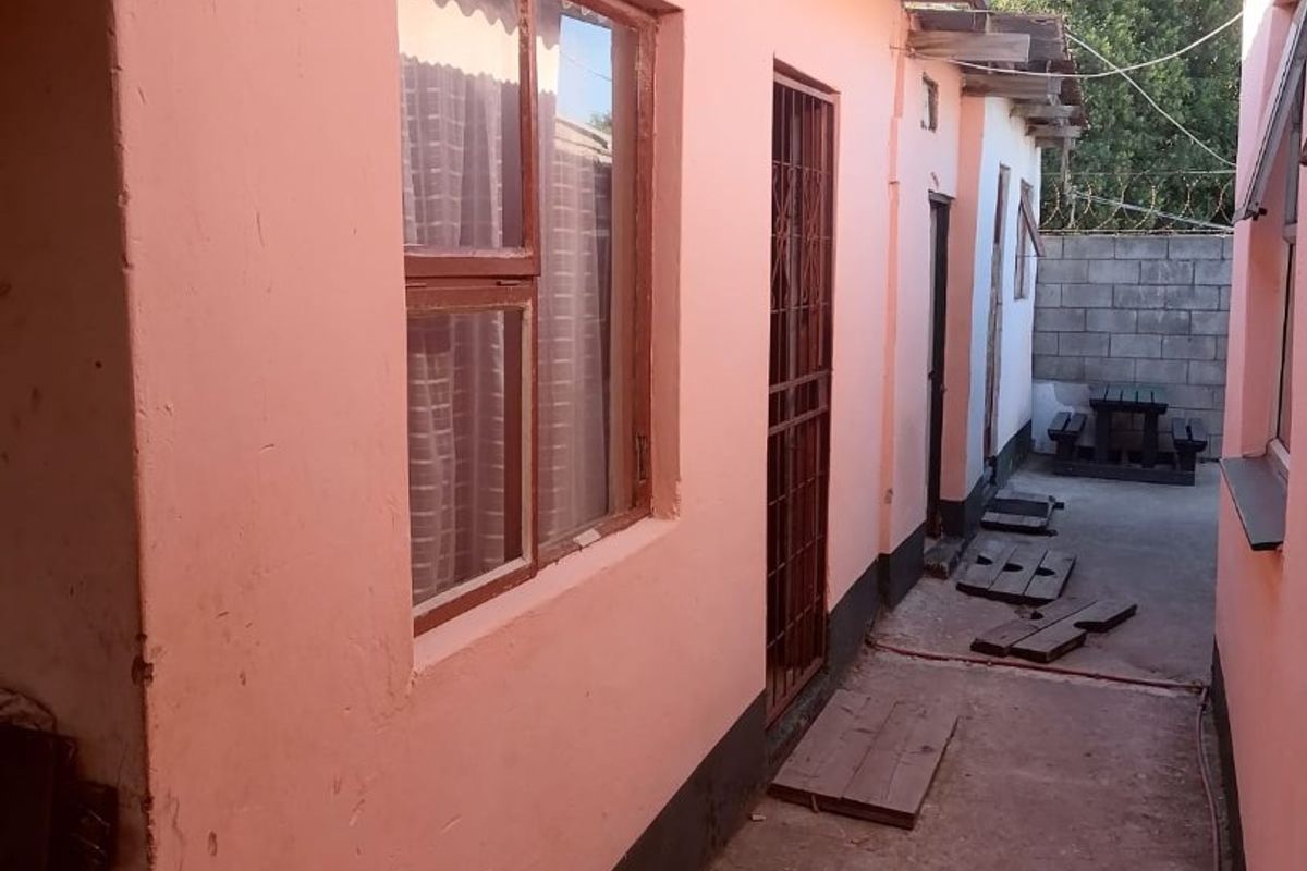 A narrow exterior side passage featuring pink painted walls, a security gate, and a concrete pathway leading to a rear courtyard area.