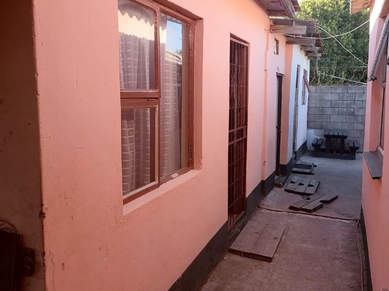 A narrow exterior side passage featuring pink painted walls, a security gate, and a concrete pathway leading to a rear courtyard area.