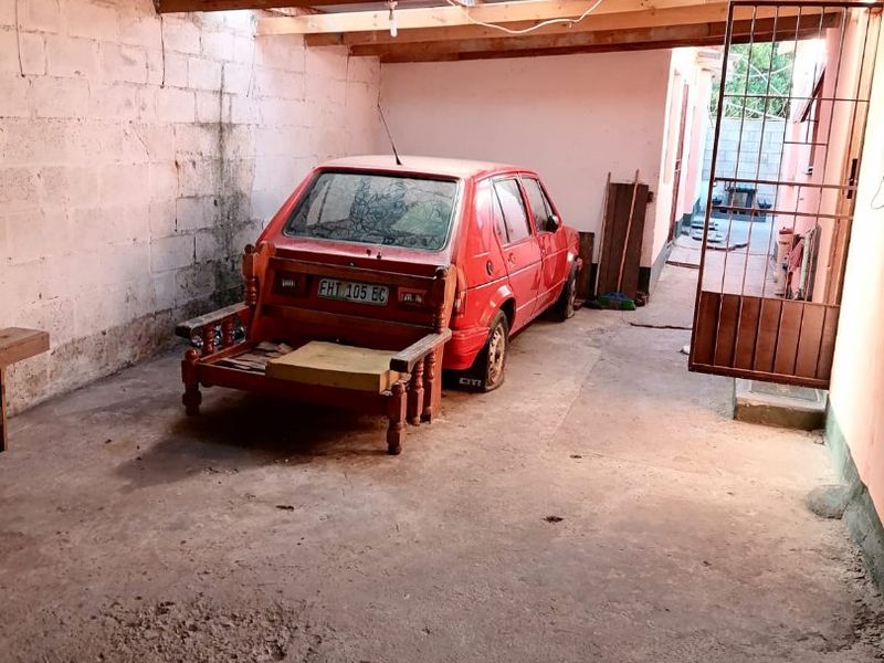 A basic, unfinished garage space featuring exposed timber rafters, corrugated roofing, and concrete flooring, providing secure covered parking or storage potential.