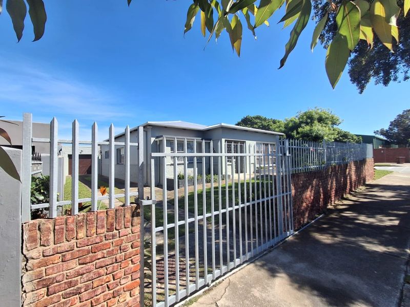 Front view of a residential property featuring a secure metal fence, brick boundary wall, concrete driveway, and attached garage.