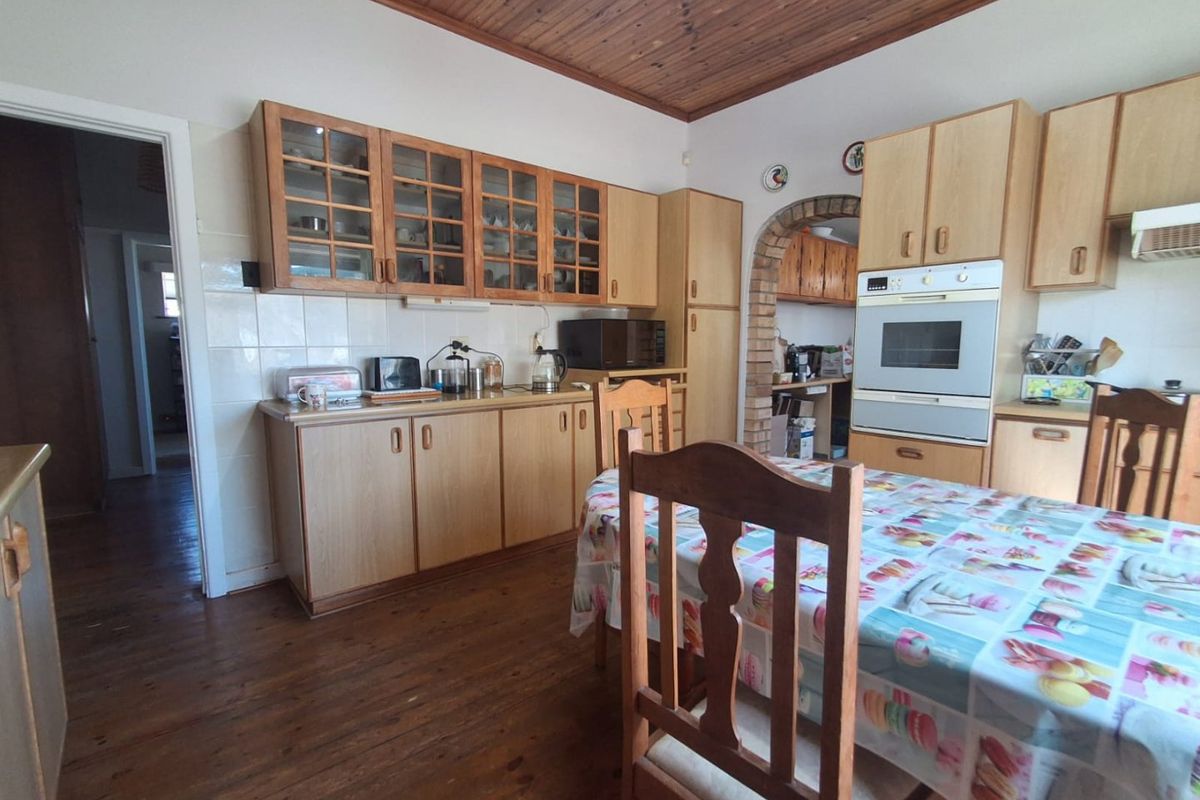 A dated kitchen featuring timber ceilings, built-in cabinetry, and a brick archway leading to a secondary prep area, with hardwood flooring throughout.