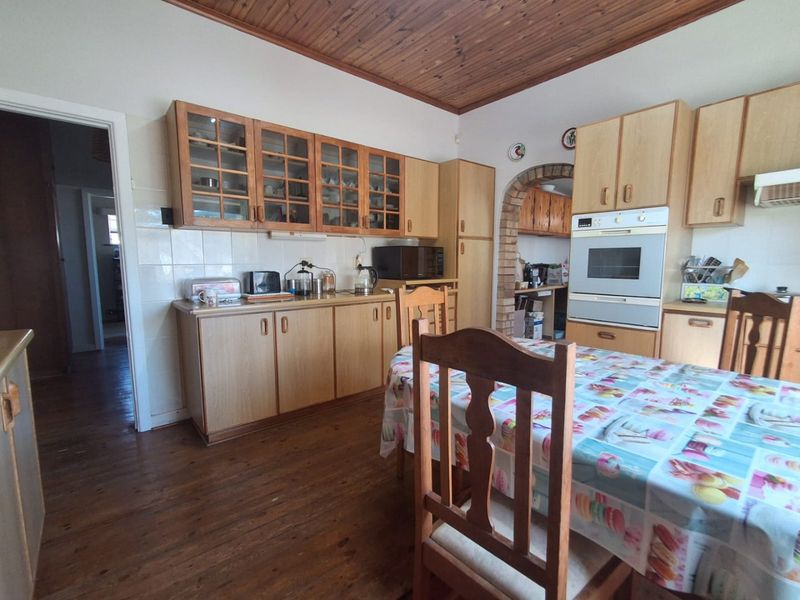 A dated kitchen featuring timber ceilings, built-in cabinetry, and a brick archway leading to a secondary prep area, with hardwood flooring throughout.