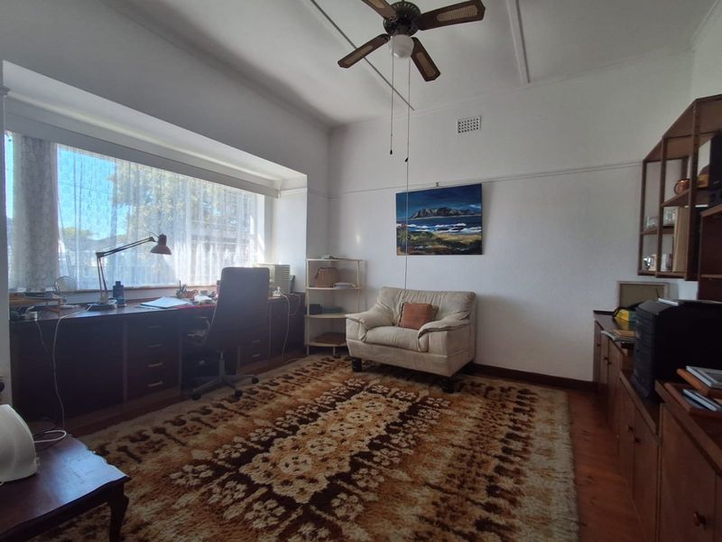 A functional home office featuring built-in desk cabinetry, timber flooring, and a ceiling fan, offering a bright workspace with large window views.