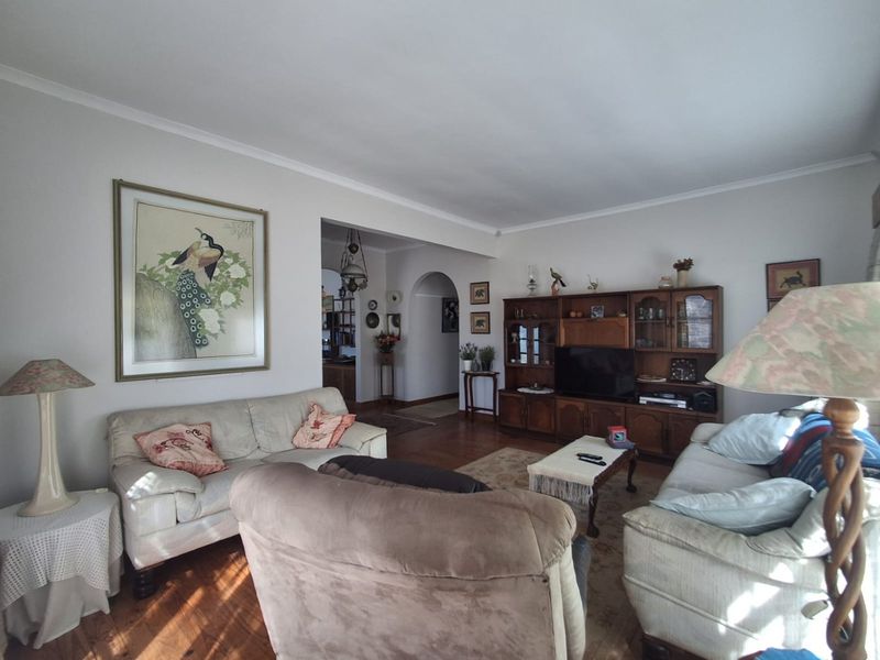 A spacious living room featuring hardwood flooring, coved cornicing, and an inviting archway leading to adjacent living areas.