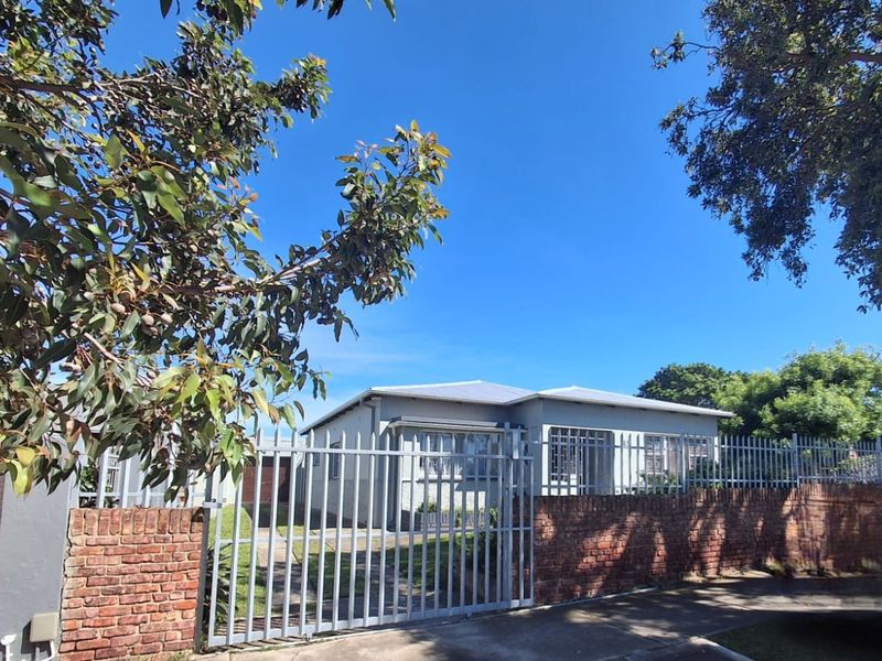 Front view of a residential house featuring a brick boundary wall, metal security fencing, and a gated driveway entrance.