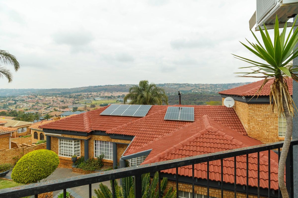 Elevated view of a residential property featuring a tiled roof with installed solar panels, brick exterior walls, and a scenic neighborhood outlook.