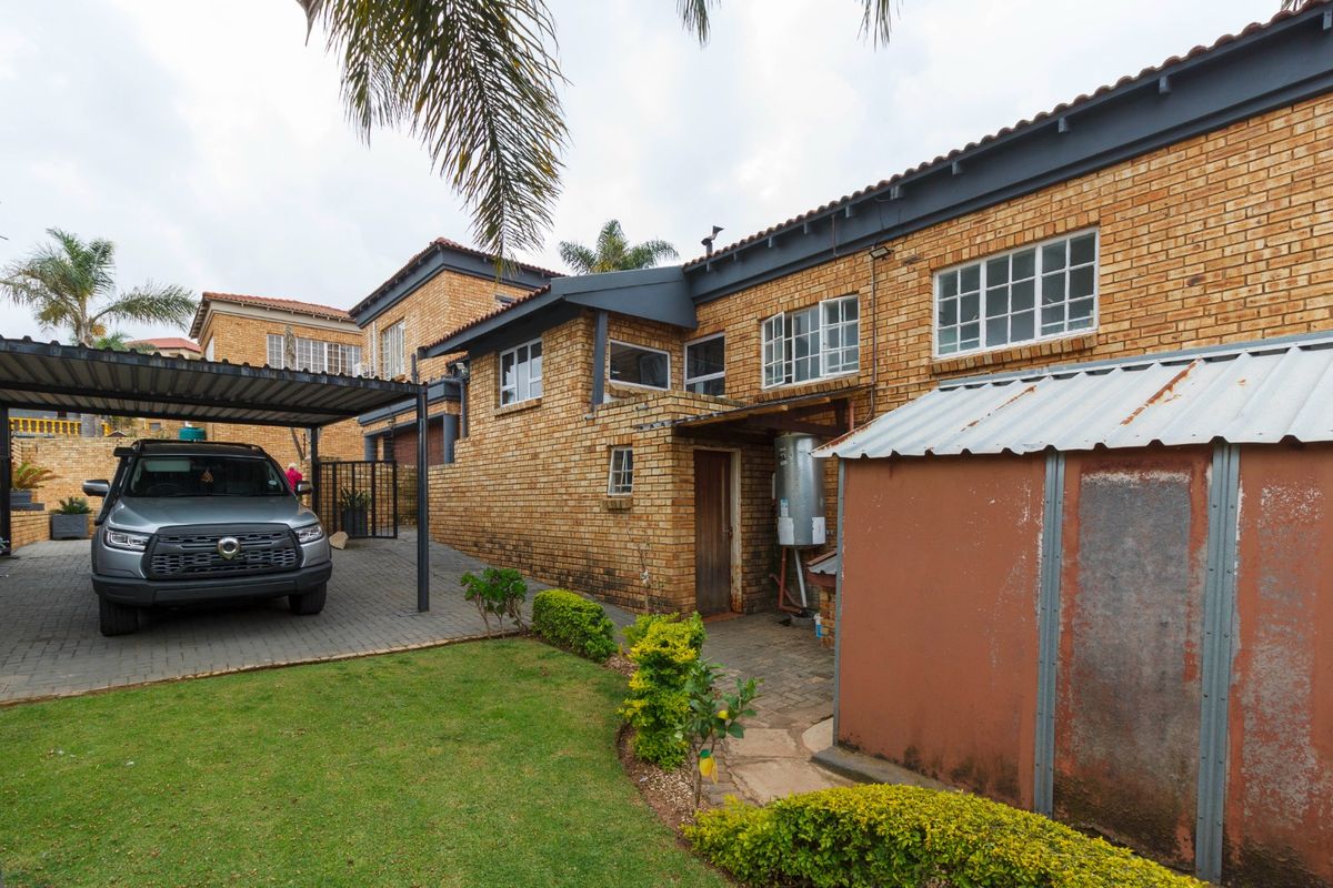 Rear exterior view of the property featuring a face brick facade, paved driveway with carport, and a metal storage shed in the garden area.