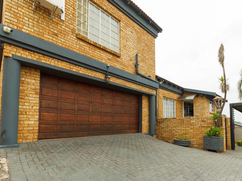 Front elevation of a double-story face brick house featuring a paved driveway and a large double garage door.